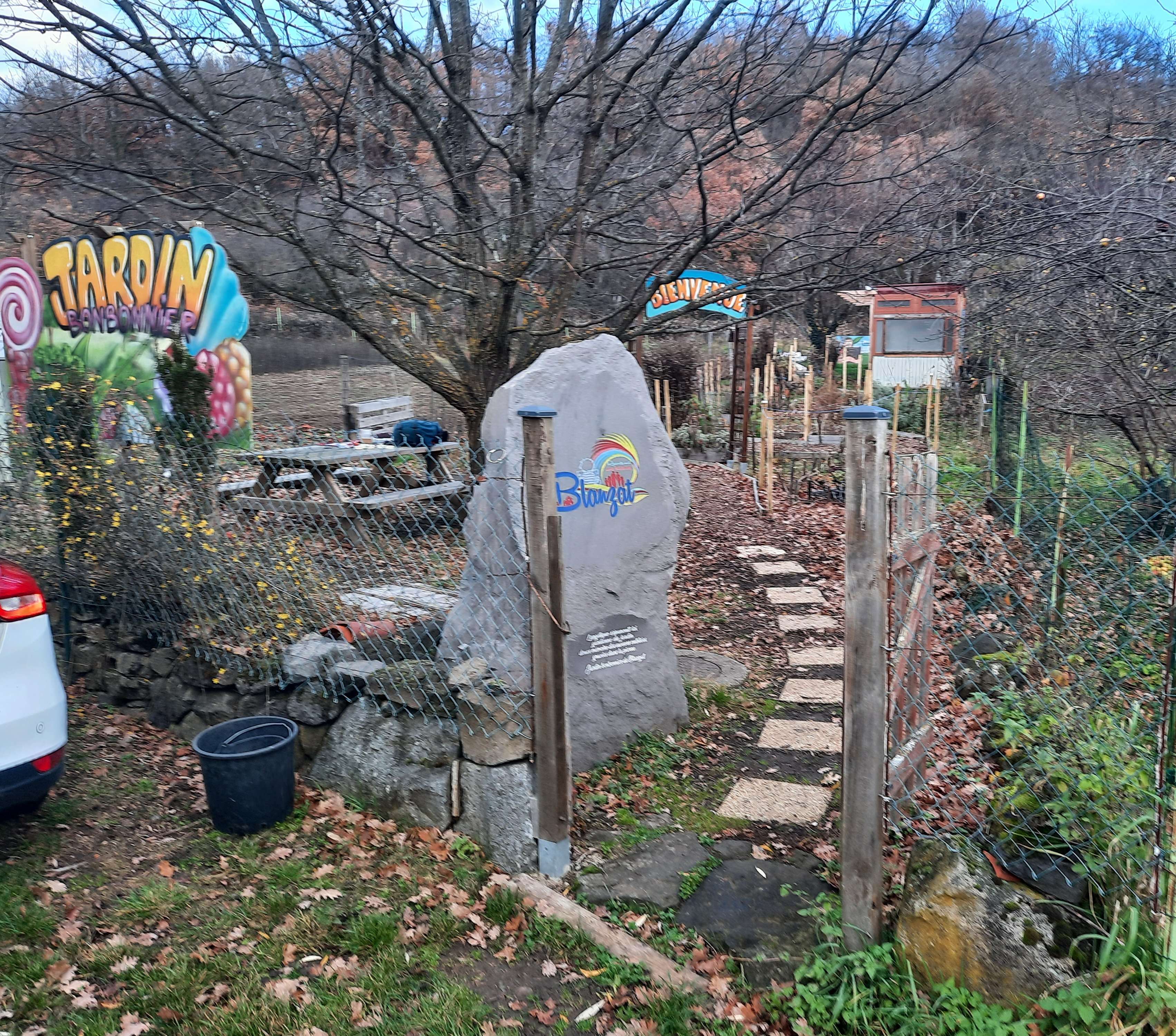 portillon ouvert, grand panneau en bois avec peint "Jardin bonbonnier", grosse pierre de Volvic avec le logo à l'entrée.